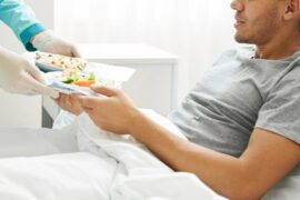 A man in a hospital bed receives a meal from a health care worker.