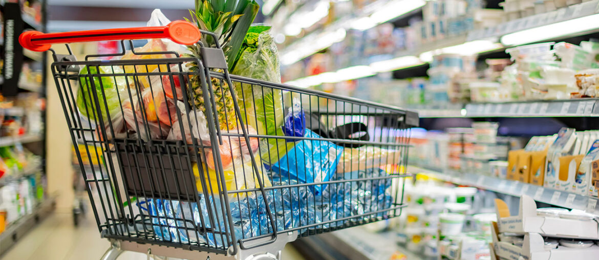 A shopping cart filled with groceries in a supermarket aisle.
