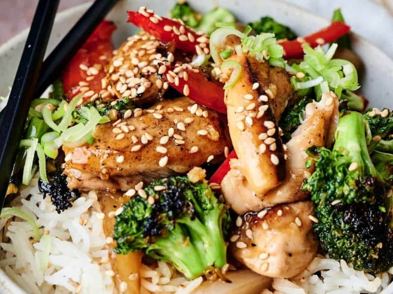 Rice bowl topped with teriyaki chicken, broccoli, peppers, and sesame.