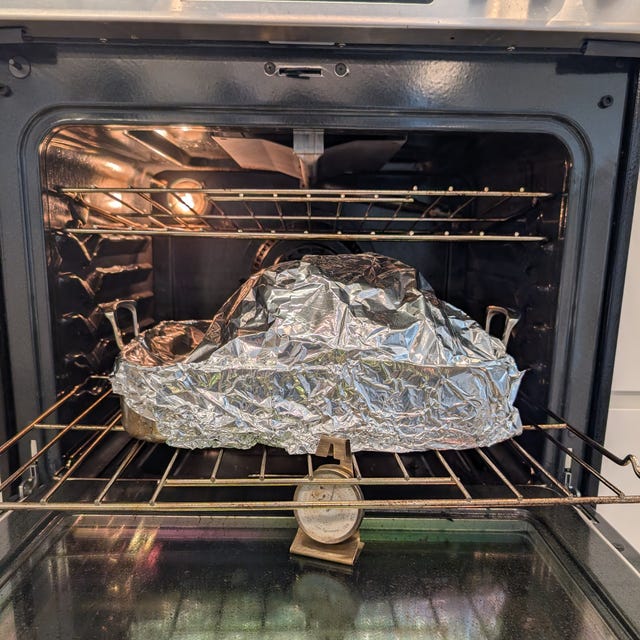 A covered dish inside an oven with a temperature gauge on the rack beneath it. A covered dish inside an oven with a temperature gauge on the rack beneath it.