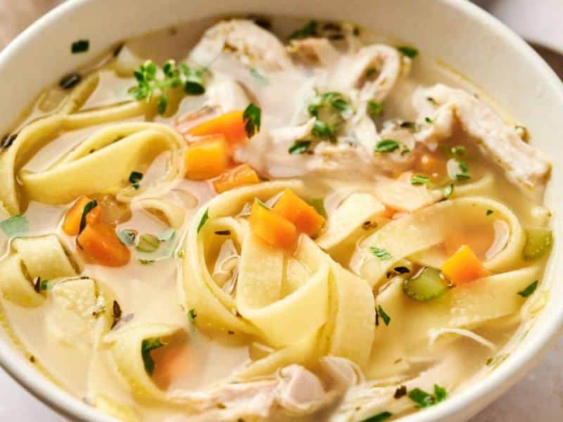 Chicken noodle soup with wide noodles, vegetables, and herbs.