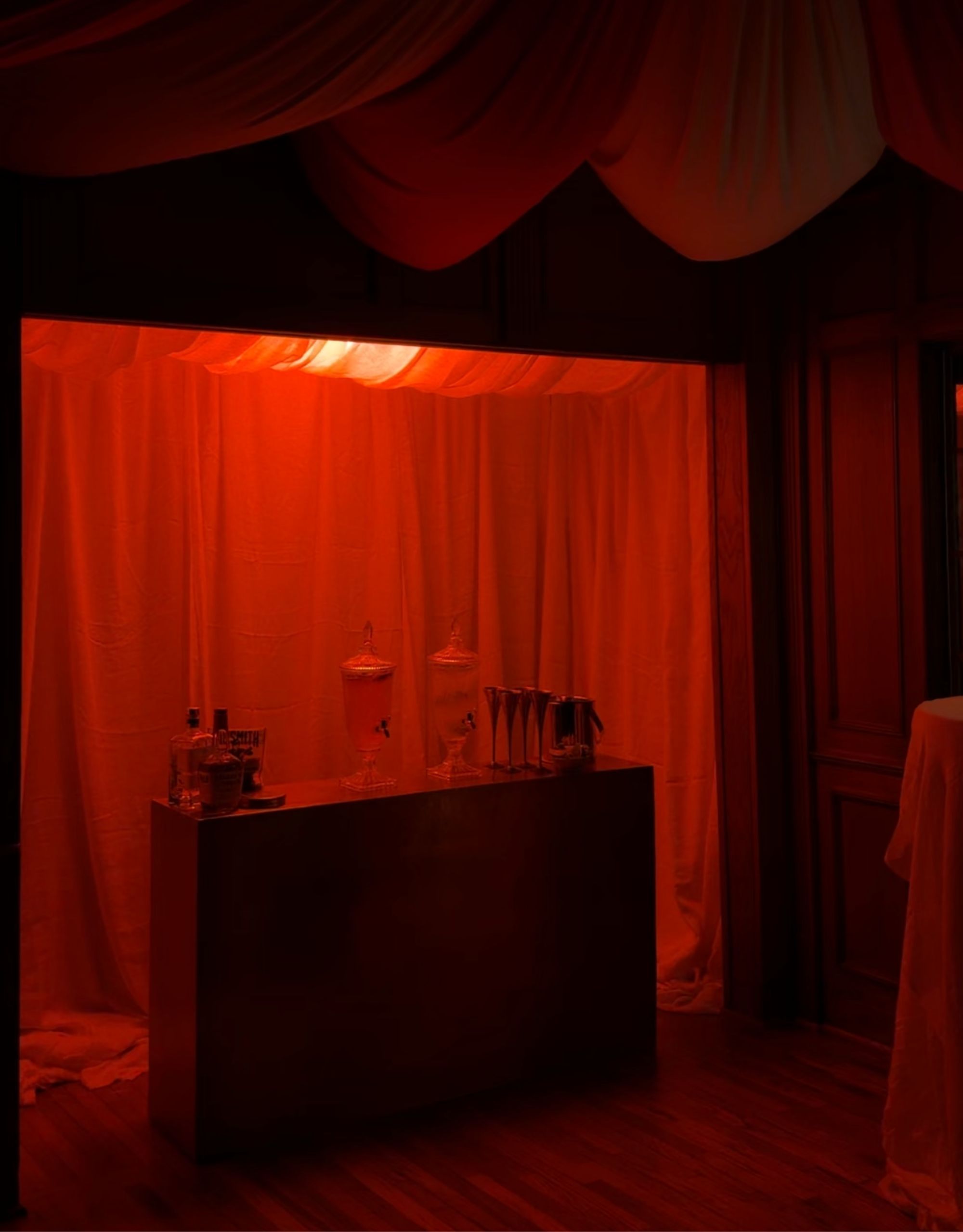 A closet bar with white fabric lining the inside lit up red with two drinks dispensers on the bar top