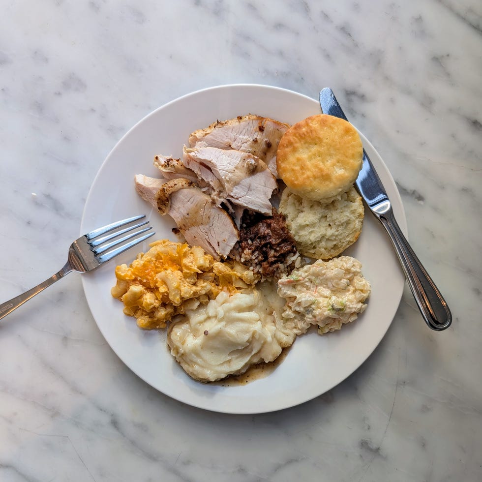 Plate of sliced turkey, biscuits, macaroni and cheese, mashed potatoes, coleslaw, and a fork and knife on a marble table. Plate of sliced turkey, biscuits, macaroni and cheese, mashed potatoes, coleslaw, and a fork and knife on a marble table.