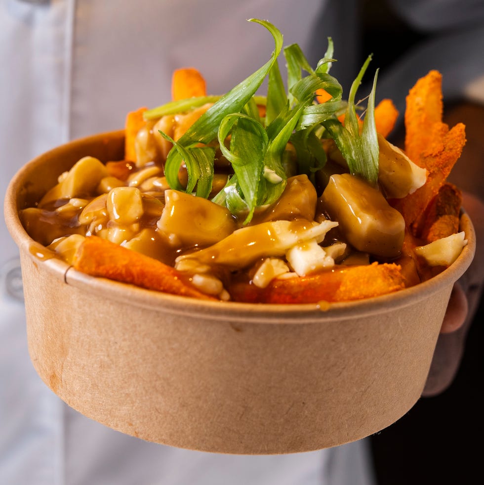 Bowl of poutine topped with green onions and served with sweet potato fries. Bowl of poutine topped with green onions and served with sweet potato fries.