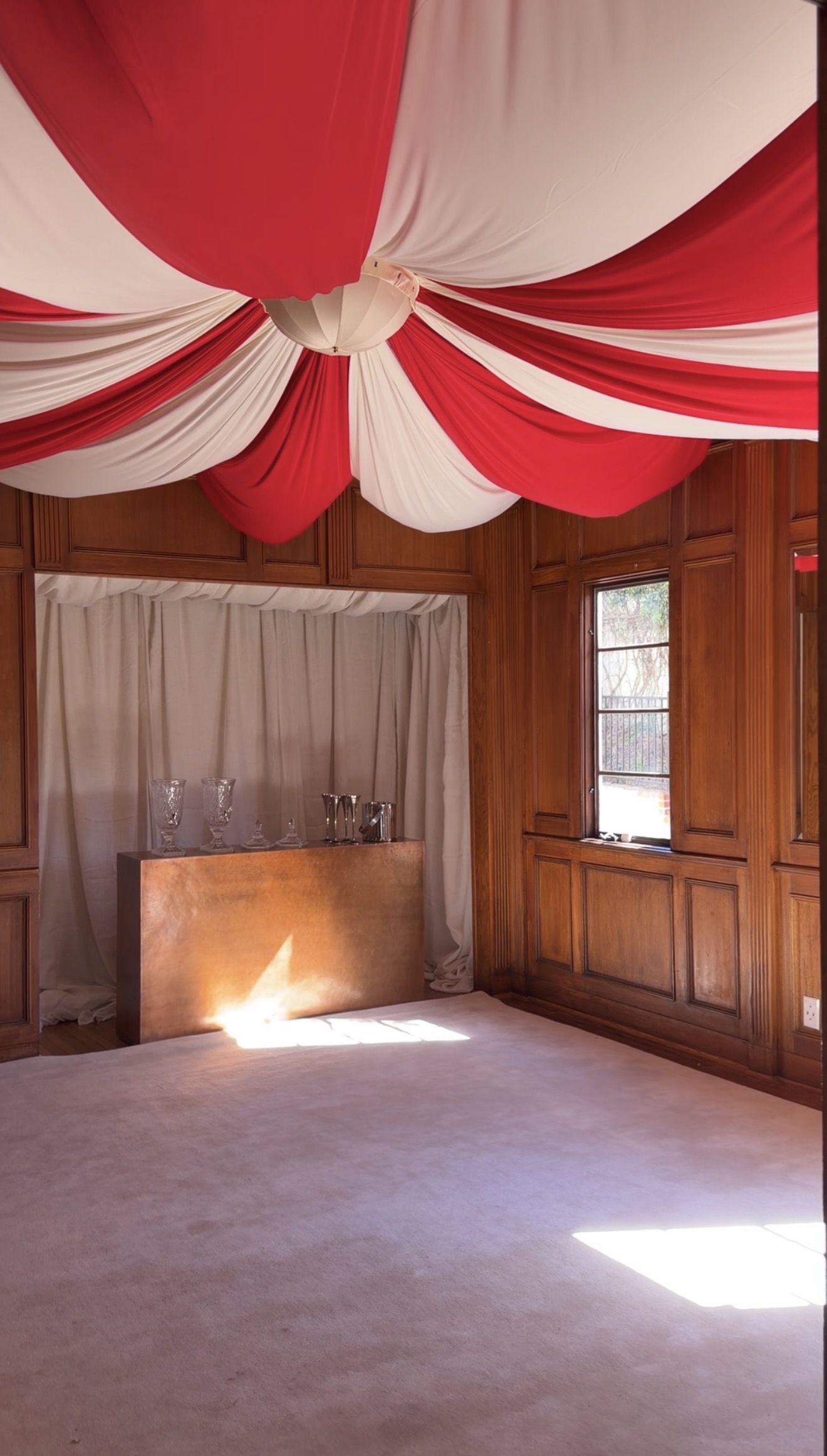 A room decorated for halloween with a tented ceiling with red and white curtain panels and a closet bar with white fabric lined inside with wood paneling all around the room